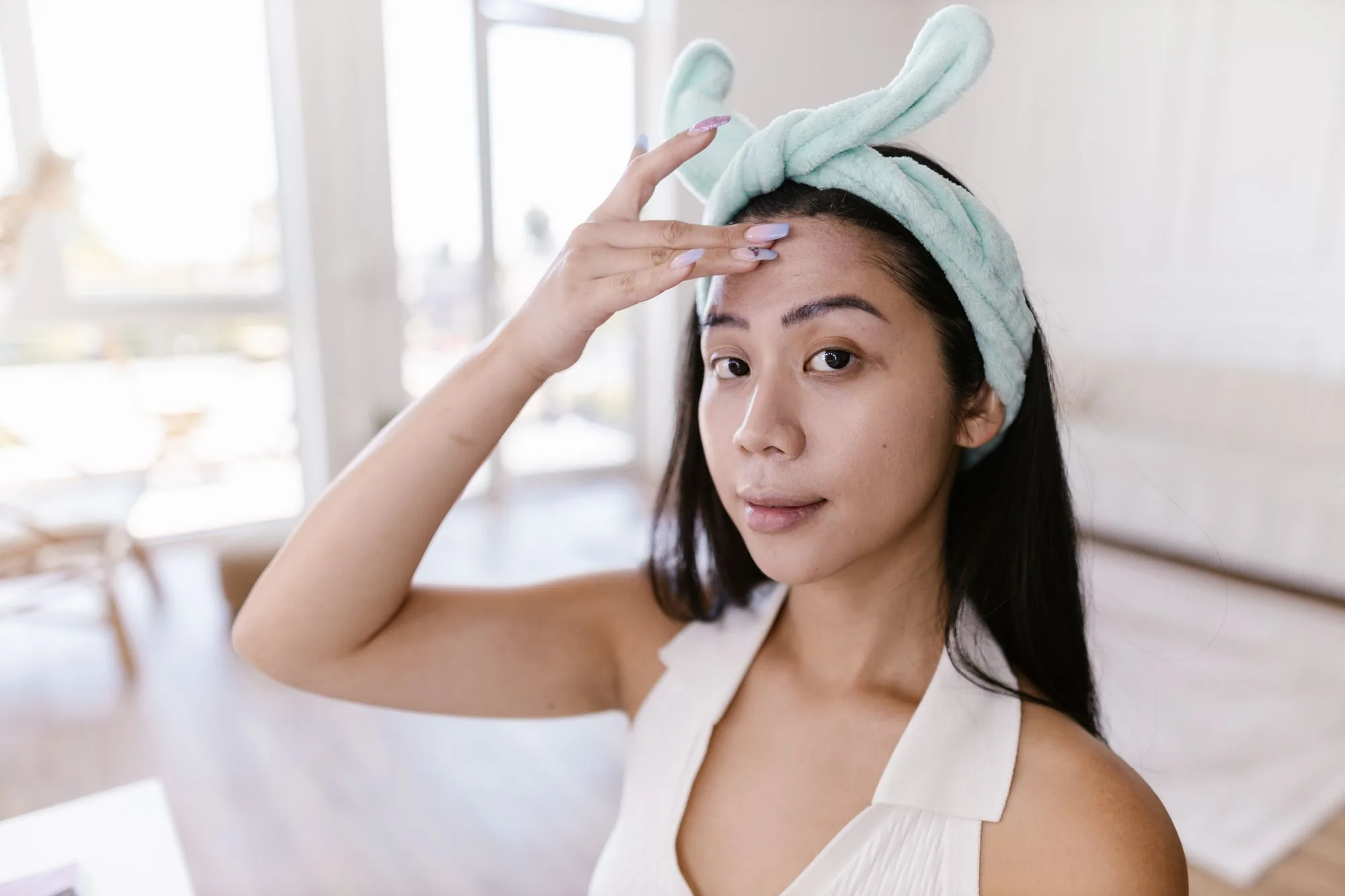 A young woman applies skincare products at home, emphasizing her daily beauty routine. Editorial photograph for our simple Japanese skincare guide for Dubai shoppers.