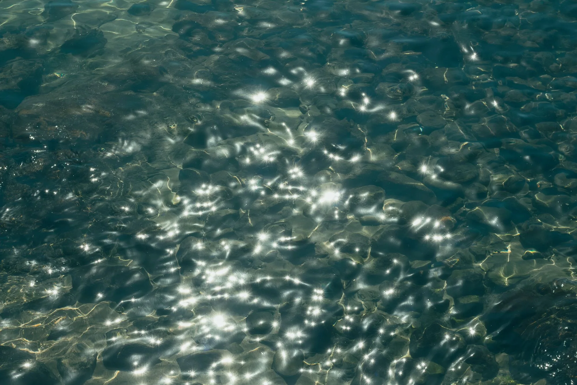 Close-up of water surface with sparkling sunlight reflections creating a serene and textured appearance. Editorial photograph for our cleansing gel guide for Dubai shoppers.