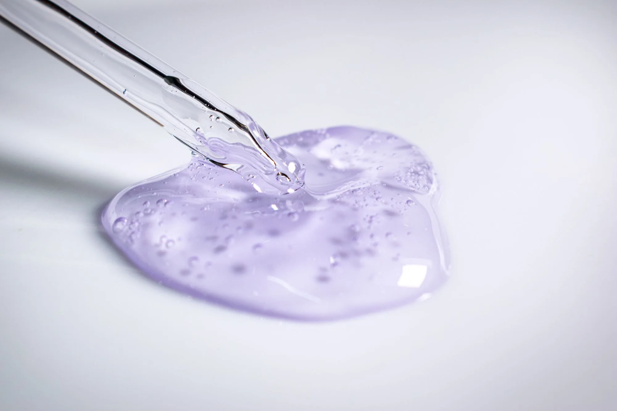 A pipette dispensing clear purple cosmetic gel onto a smooth surface. Editorial photograph for our skincare ingredient list guide for Dubai shoppers.
