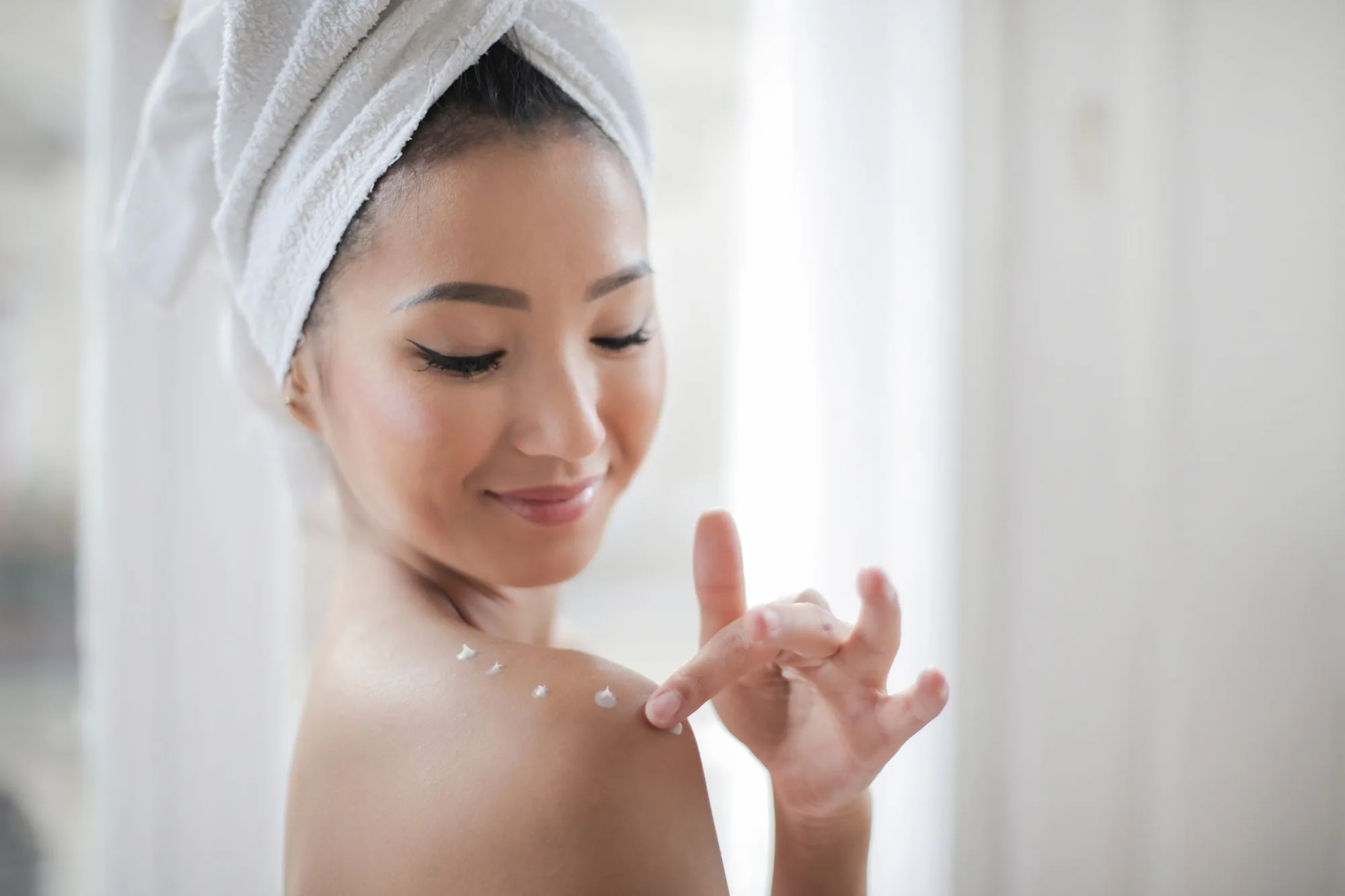 A young woman applying moisturizer indoors, enhancing skin care routine. Editorial photograph for our Japanese skincare routine guide for Dubai shoppers.