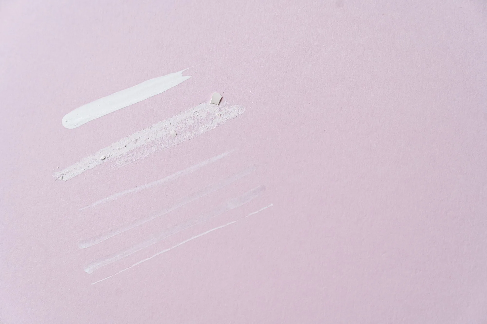 Flat lay of skincare product swatches on a pastel pink background, ideal for beauty and cosmetics themes.