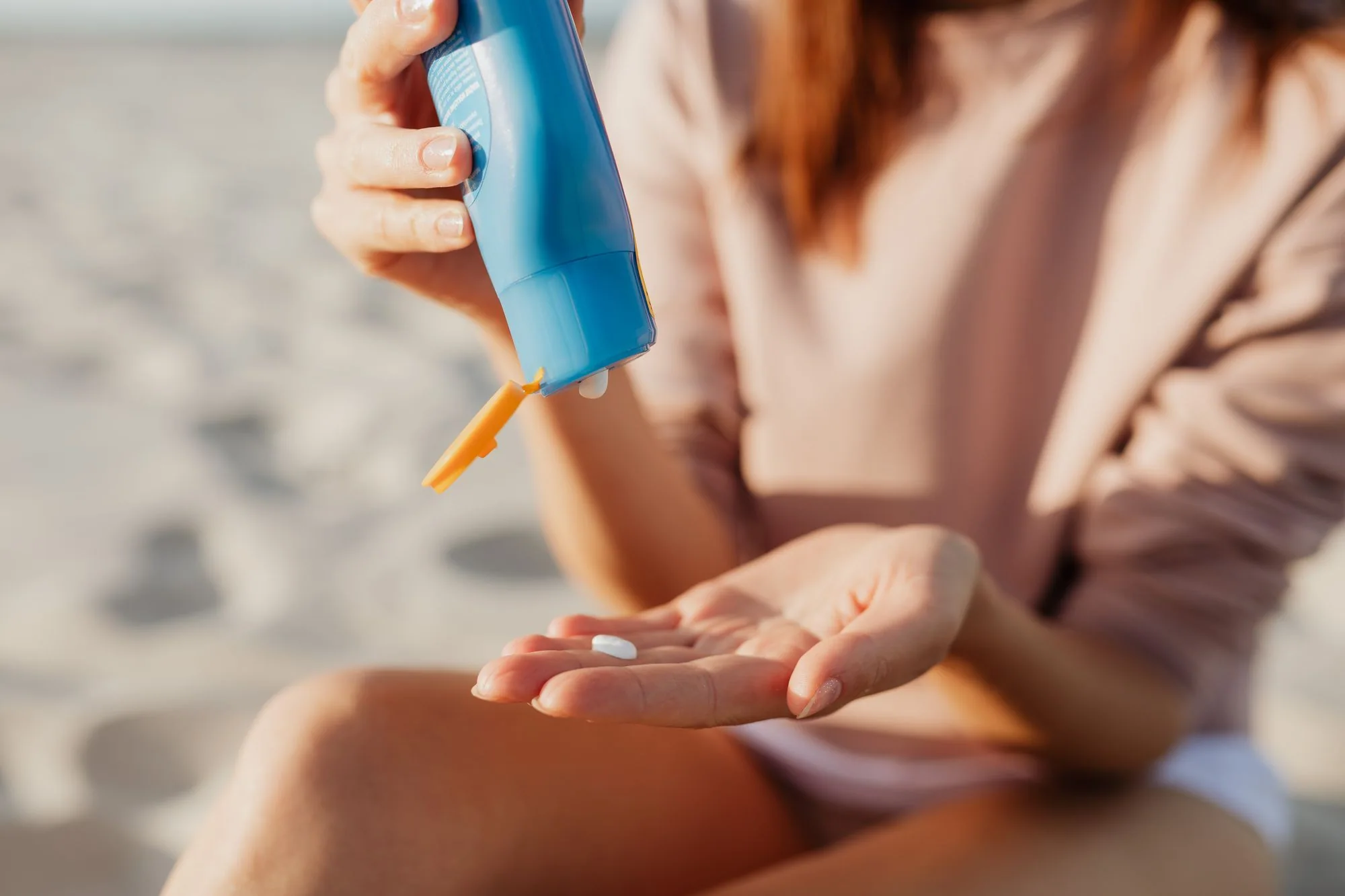 A person applies sunscreen at the beach on a sunny day. Editorial photograph for our SPF50+ guide for Dubai shoppers.