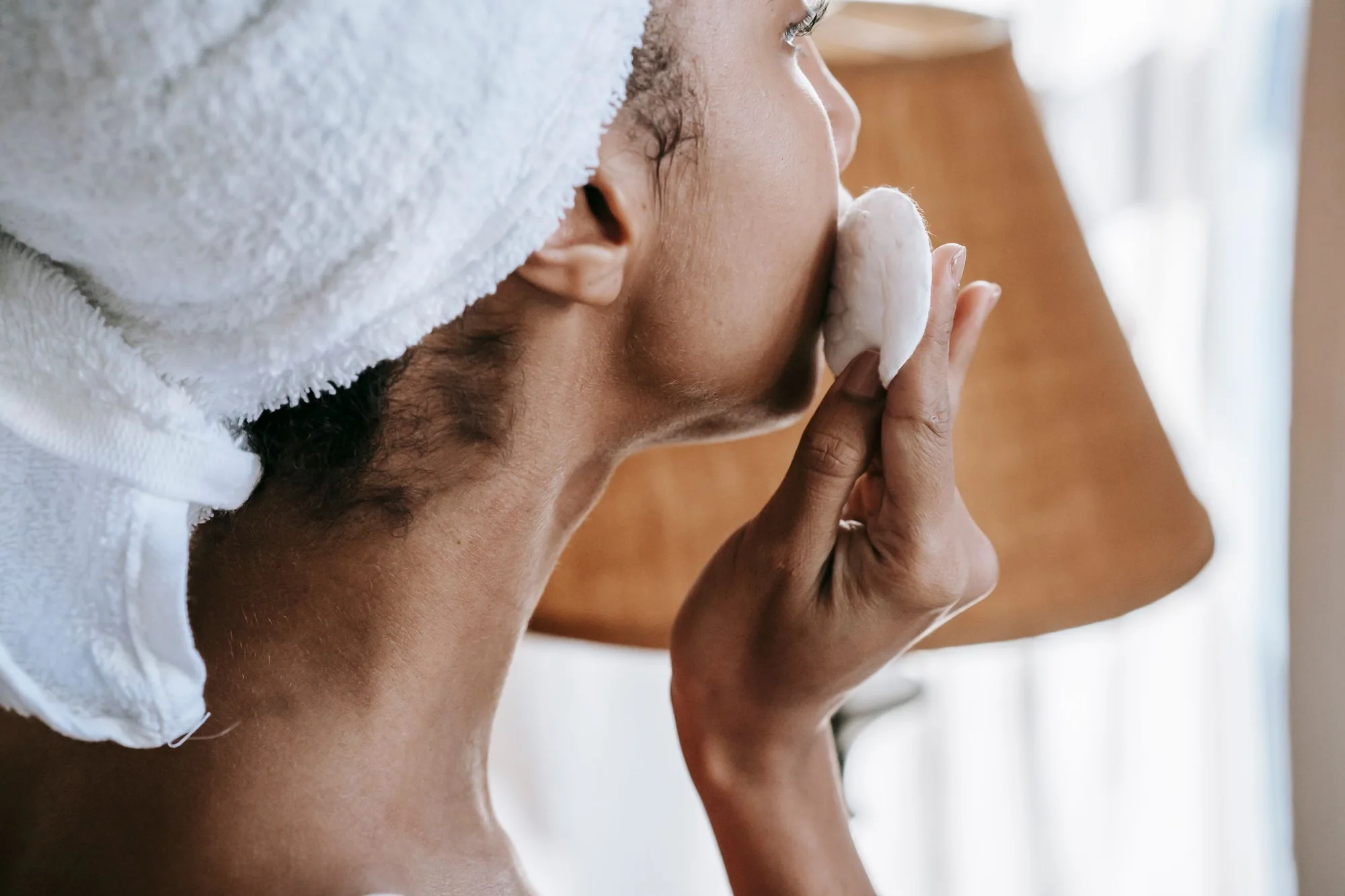 Woman with towel on head applying skincare product at home, creating a calm, serene atmosphere.