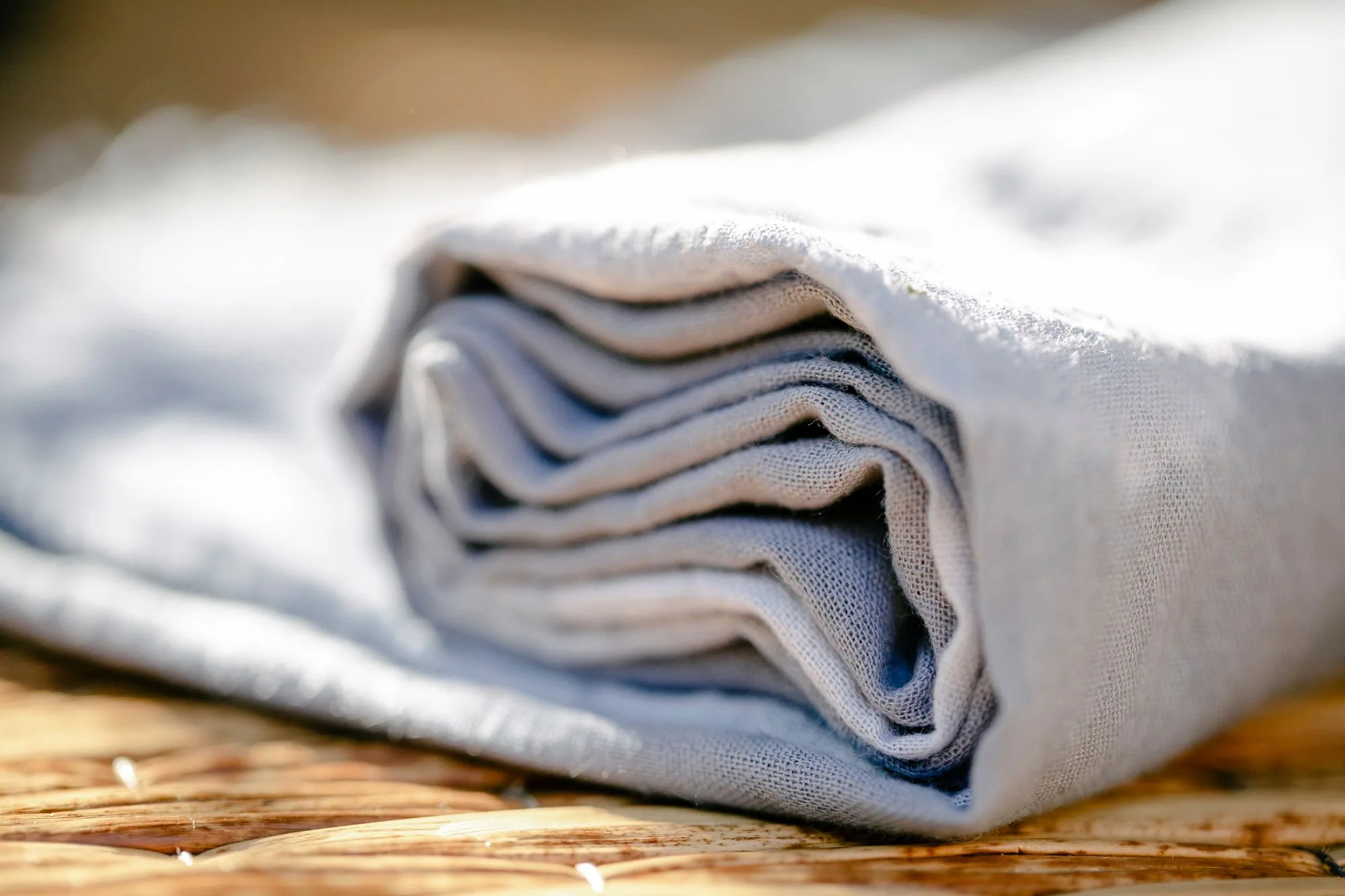 A detailed shot of a neatly folded linen fabric showcasing its texture and craftsmanship on a wicker surface.