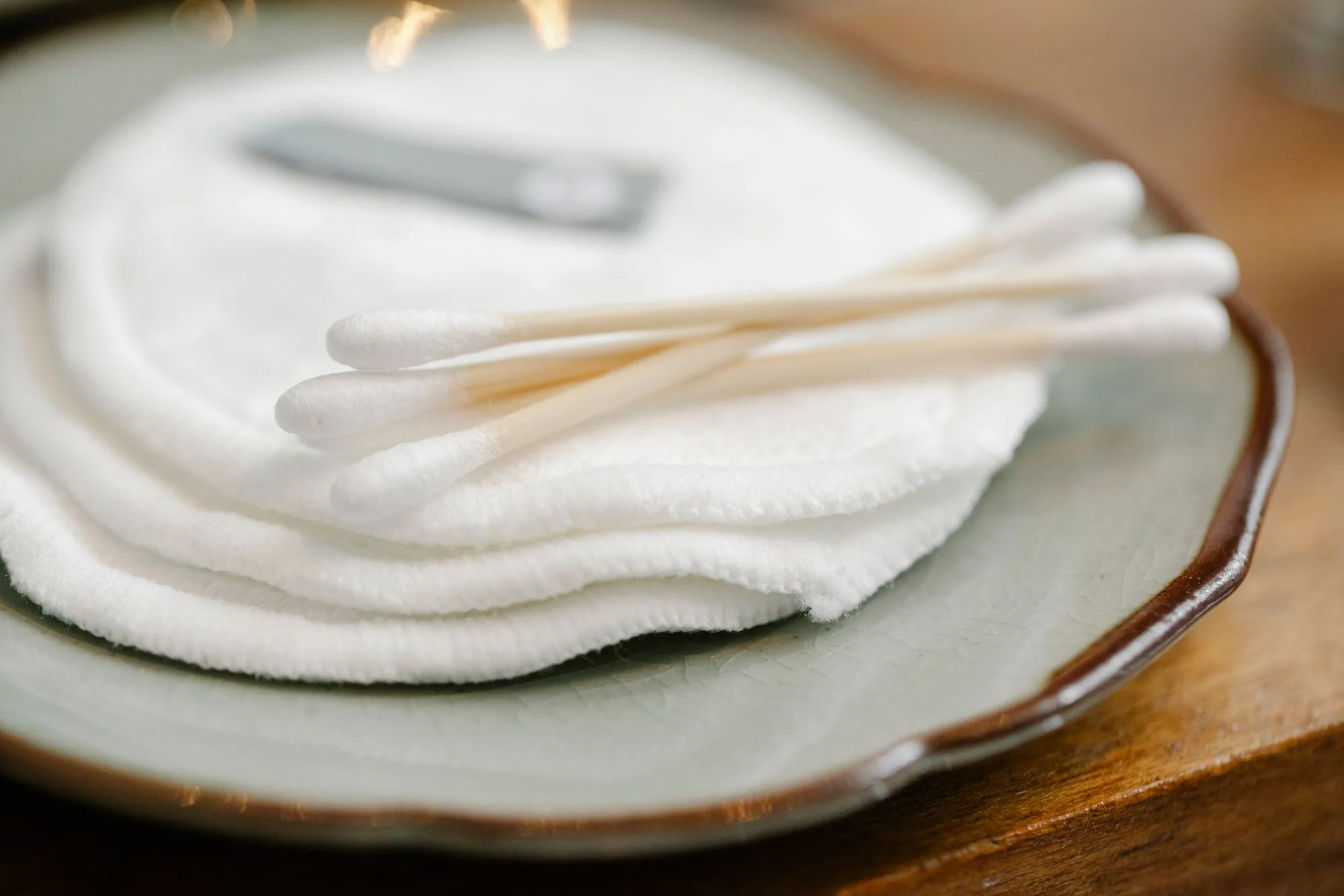 Close-up of white cotton pads and swabs on a decorative ceramic plate for personal skincare routine.
