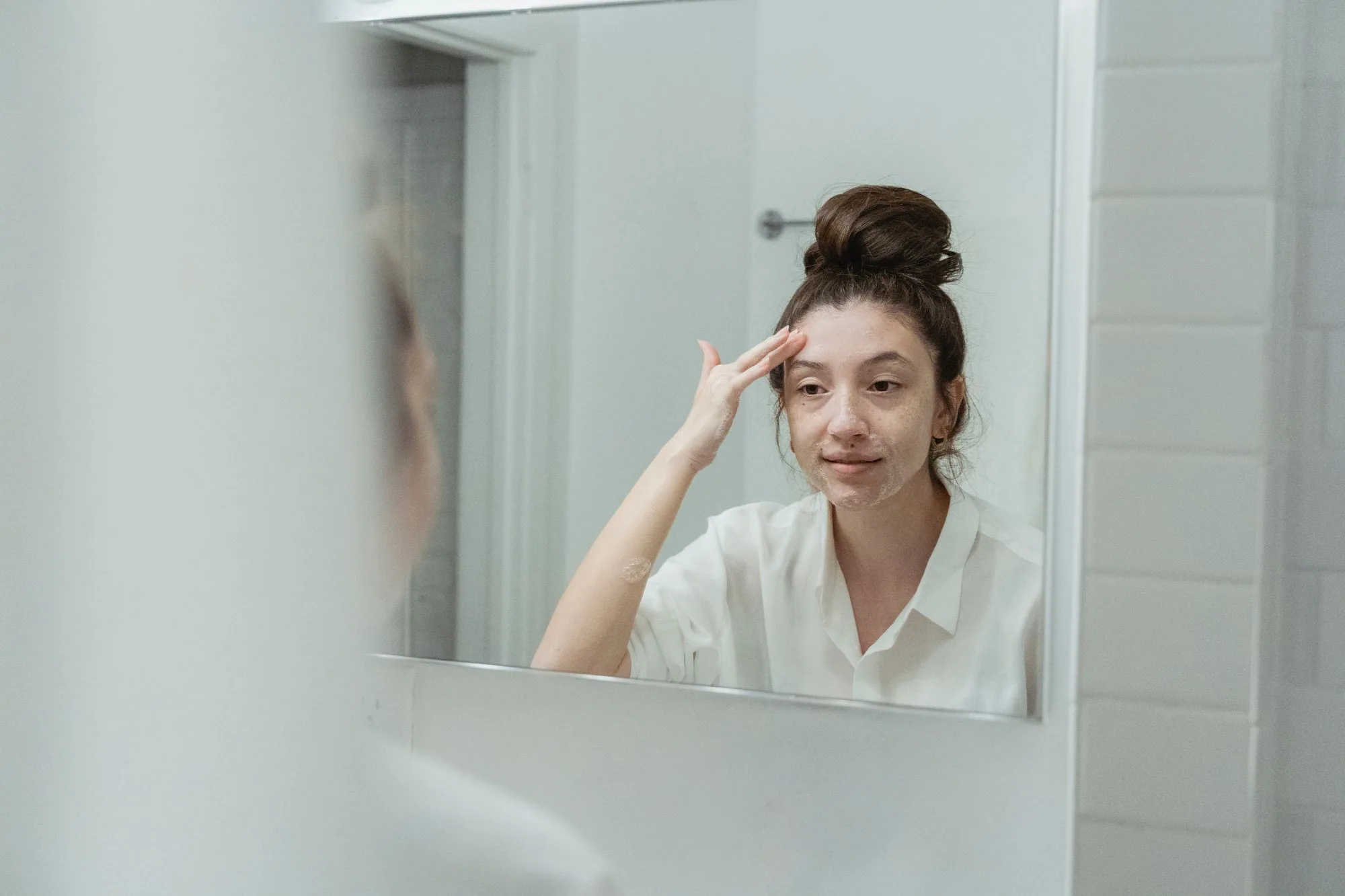 Woman in bathroom applying facial cream, reflecting self-care and relaxation. Editorial photograph for our evening skincare guide for Dubai shoppers.
