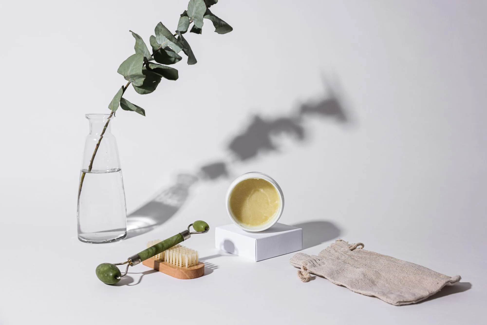 Aesthetic studio shot of skincare products including a jade roller, brush, and cream jar with eucalyptus branch. Editorial photograph for our AGTHEORY guide for Dubai shoppers.