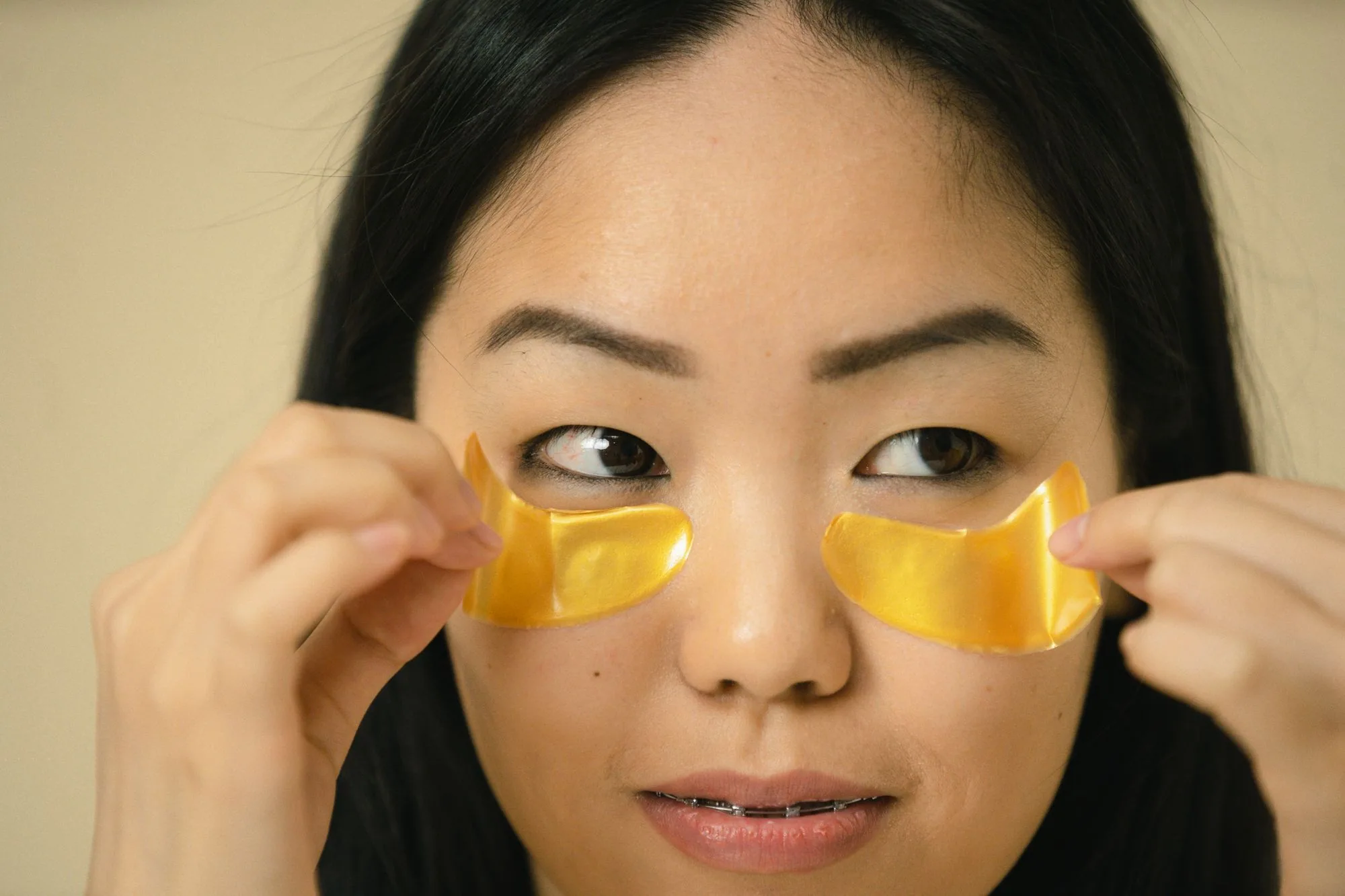 Close-up of an Asian woman applying gold under-eye patches for skincare routine. Editorial photograph for our skincare before an event guide for Dubai shoppers.