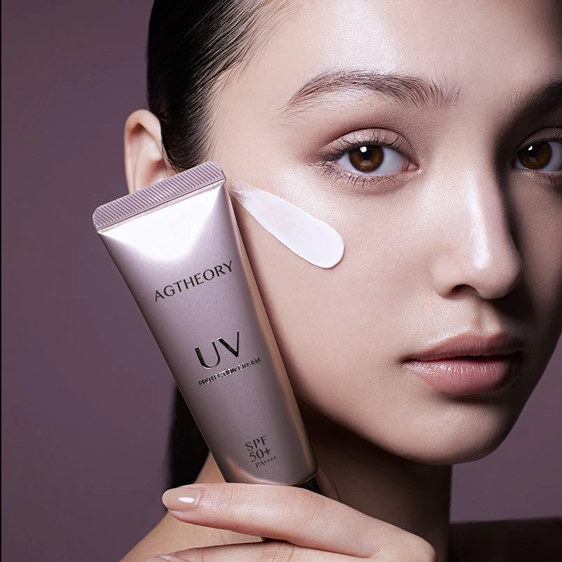 A model holding AGTHEORY كريم الحماية من الشمس with cream on her cheek